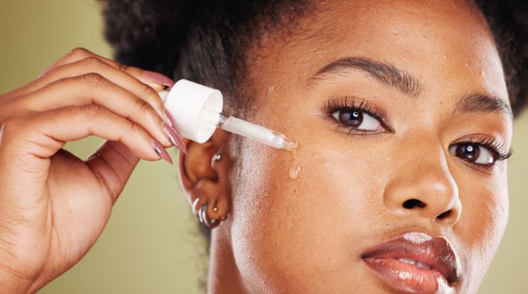 Mulher negra aplicando um sérum de retinol na pele do rosto