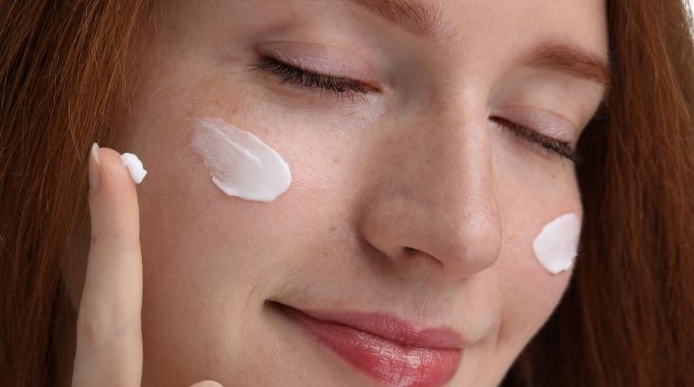 Jovem negra sorridente ao tirar manchas da pele facial com o uso de cremes e séruns em sua rotina.