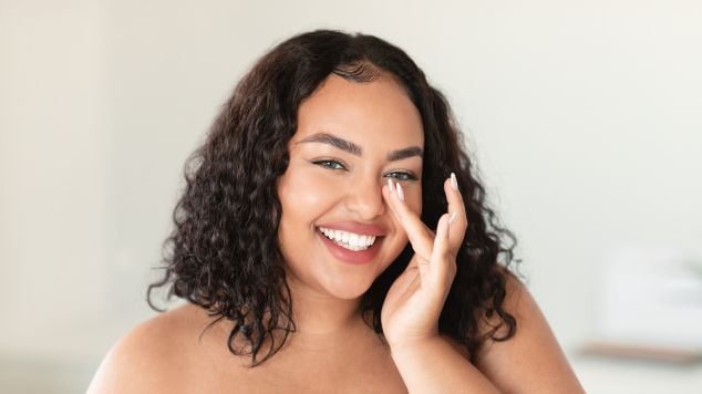 Jovem mulher sorridente usa um hidratante facial combinando colágeno com ácido hialurônico