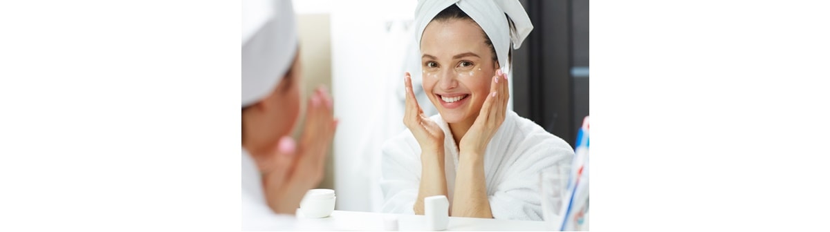 Mulher caucasiana sorri ao aplicar o creme de hidratação em seu rosto