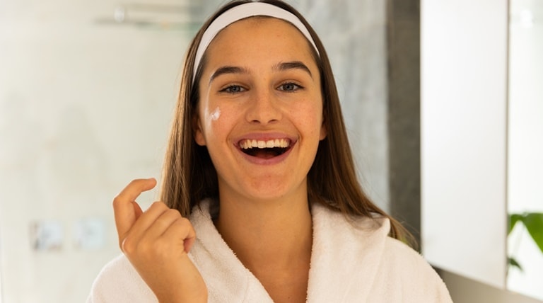 Jovem sorridente utiliza creme hidratante para hidratar sua pele facial