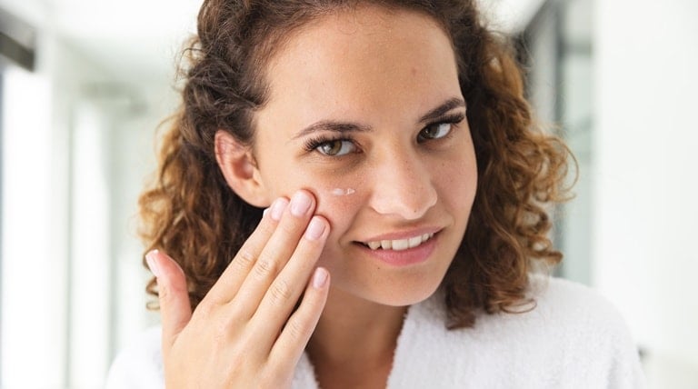 Mulher aplica hidratante para pele facial em seu rosto