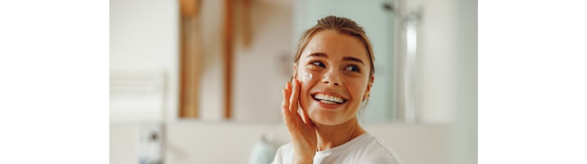 Jovem mulher sorridente aplica um creme facial em seu rosto