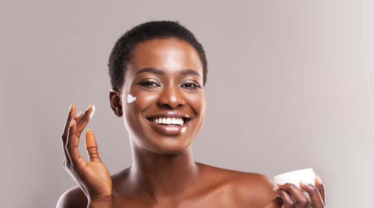 Jovem mulher sorri ao aplicar seu creme de hidratação para hidratar a pele do rosto