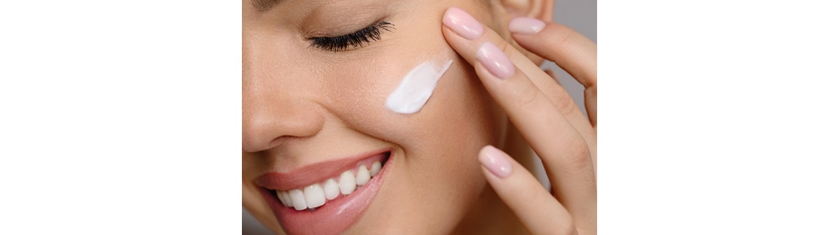 Mulher aplica creme hidratante facial em sua bochecha enquanto sorri