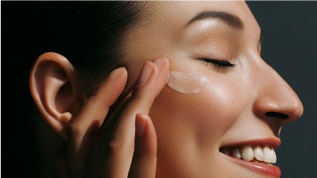 Jovem mulher caucasiana aplica creme hidratante para o rosto em sua pele facial