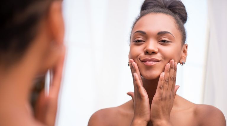Garota sorridente aplica um hidratante de rosto em sua pele facial