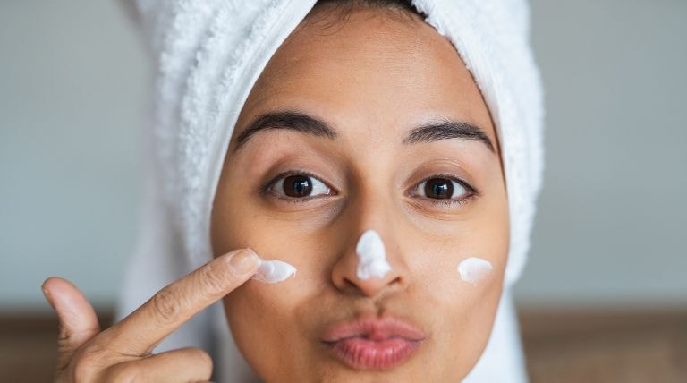 Mulher alegre utiliza creme hidratante que pode ser de uso diurno e noturno