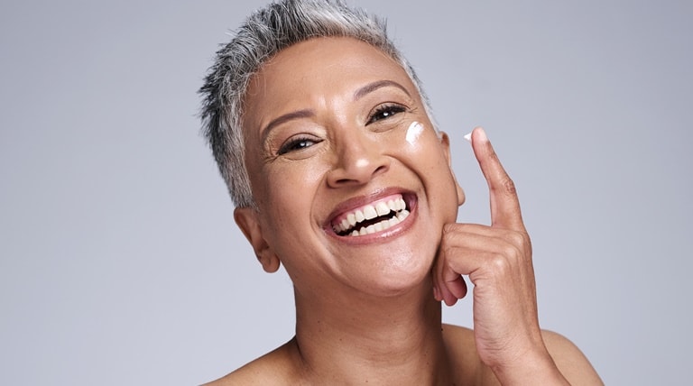 Mulher com mais de 40 anos aplica creme para hidratar o rosto com a pele madura