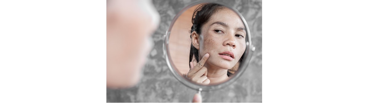 Mulher asiática observa sua pele facial ao considerar usar um creme para tirar manchas no rosto