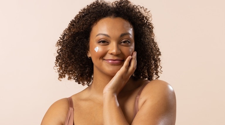 Mulher negra toca sua pele com creme para hidratação facial