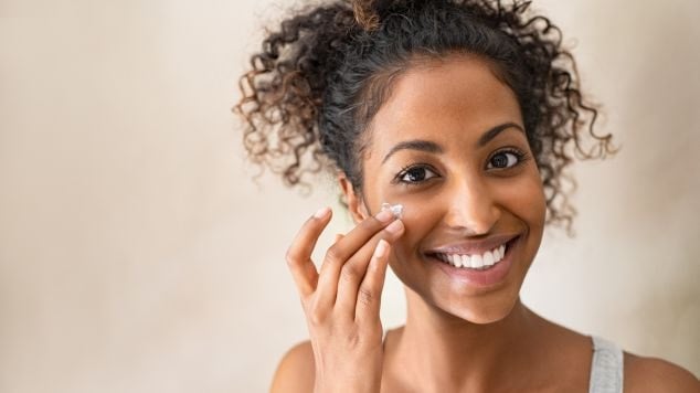 mulher jovem sorrindo enquanto passa hidratante facial