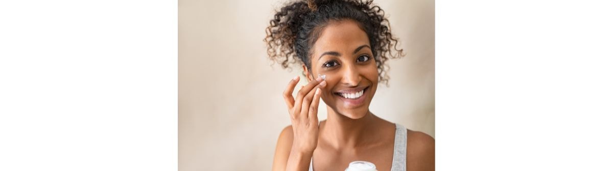 mulher jovem sorrindo enquanto passa hidratante facial