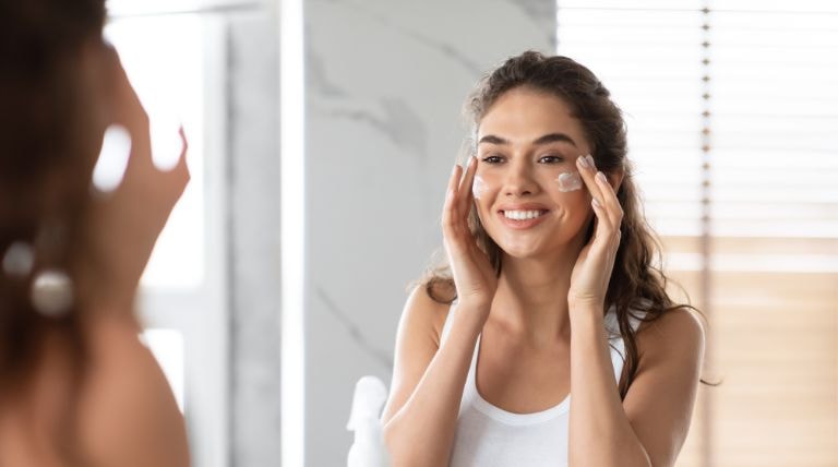 Mulher observa a si mesma no espelho ao aplicar hidratante facial para pele oleosa em seu rosto 