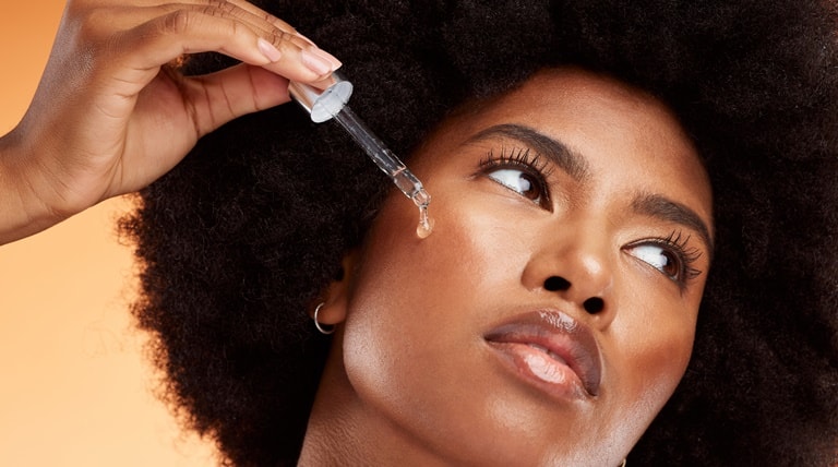 Jovem negra aplica o sérum facial em sua pele do rosto