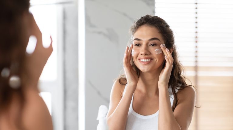 Mulher observa a si mesma no espelho ao aplicar hidratante facial para pele oleosa em seu rosto