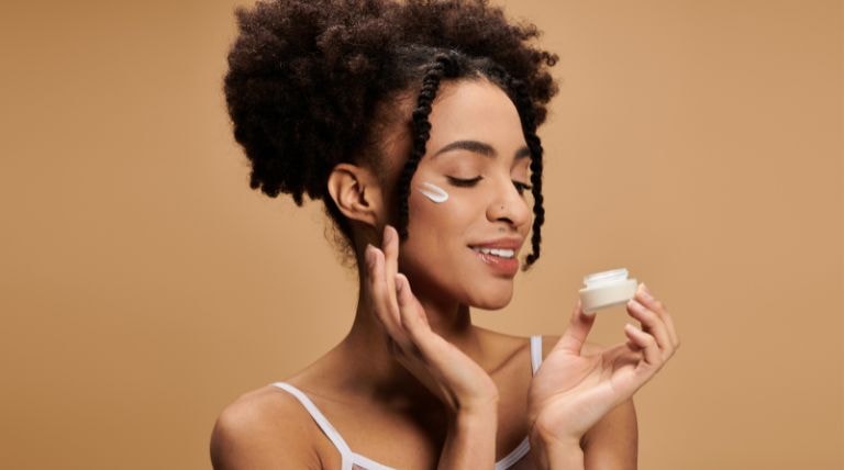 Jovem negra aplica hidratante facial suavemente na pele do rosto.