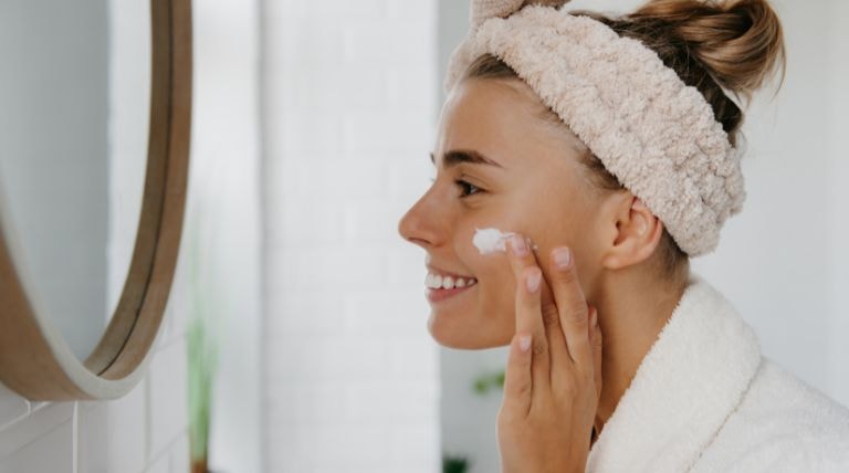 Mulher adulta caucasiana aplicando hidratante facial no rosto para pele sensível