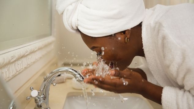 Mulher negra abaixada sobre a pia para lavar o rosto com um gel de limpeza do rosto