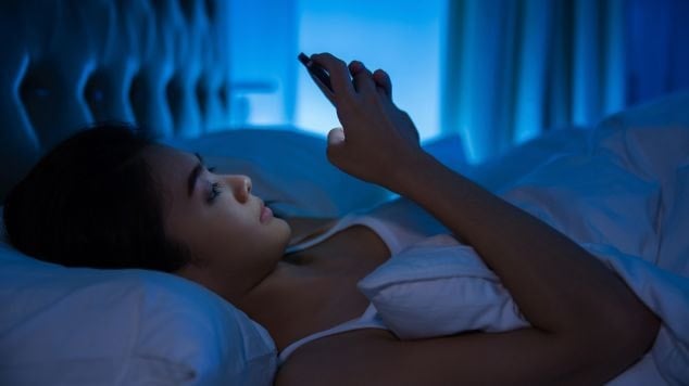 Mulher utiliza celular antes de dormir, se expondo aos problemas da luz azul na rotina