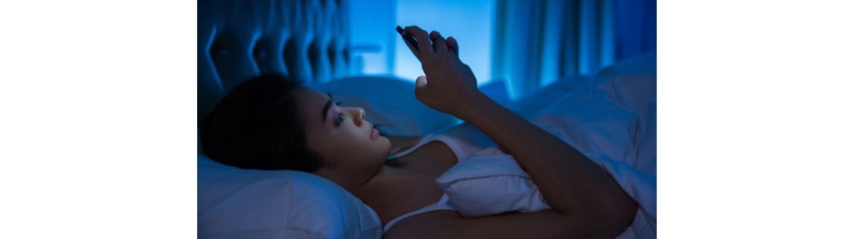 Mulher utiliza celular antes de dormir, se expondo aos problemas da luz azul na rotina