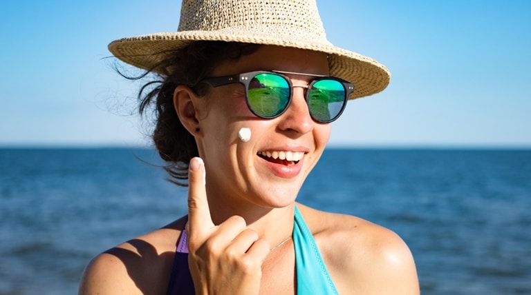 Mulher caucasiana  em frente ao mar aplica o protetor solar facial para proteger a pele de seu rosto