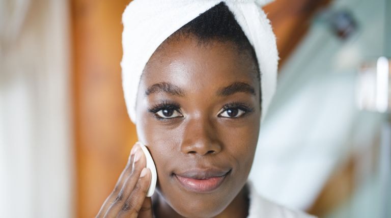 Jovem mulher negra utiliza água micelar em seu kit de limpeza de pele