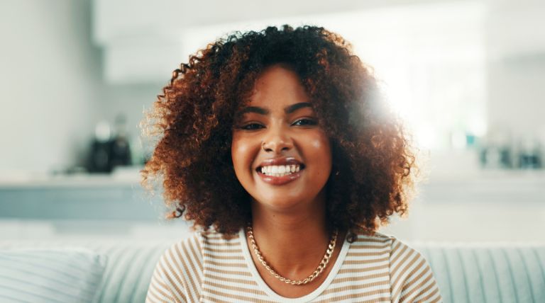 Mulher sorridente com o cabelo crespo de cor marrom chocolate com luzes sutis e suaves.