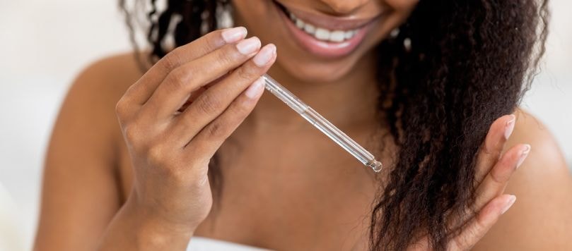 Jovem negra aplica gotas do óleo de abacate para nutrir e hidratar o cabelo.