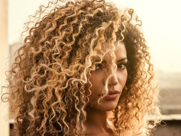 Mulher com cabelo cacheado de cor loiro manteiga dourado