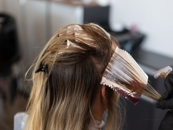 Profissional realiza a descoloração para pintar o cabelo de sua cliente com a cor loiro manteiga.