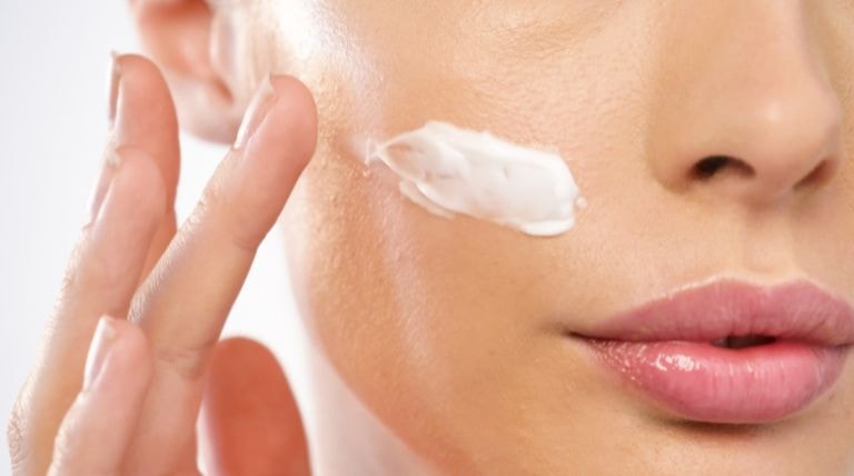 Mulher aplica um hidratante com ácido hialurônico em sua pele do rosto como parte de sua rotina de skincare.