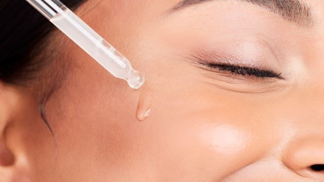 Mulher sorridente aplica um sérum facial com ácido hialurônico em sua pele do rosto