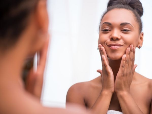 Jovem negra aplica um hidratante facial de toque seco com ácido salicílico para tratar a acne em sua pele facial.