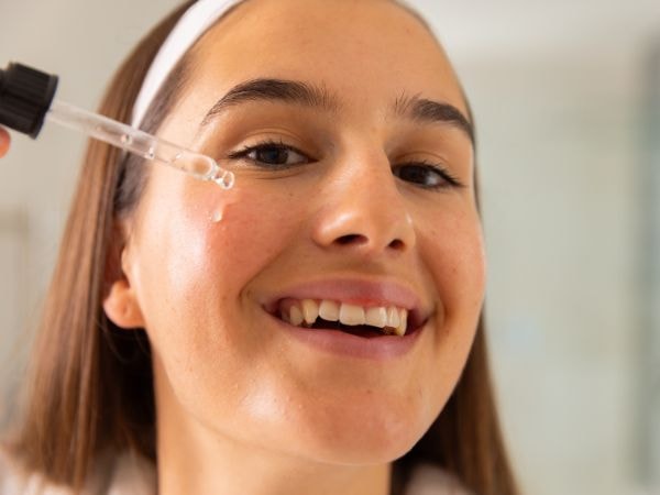 Mulher sorridente aplica um sérum antiacne com ácido salicílico para combater a acne.