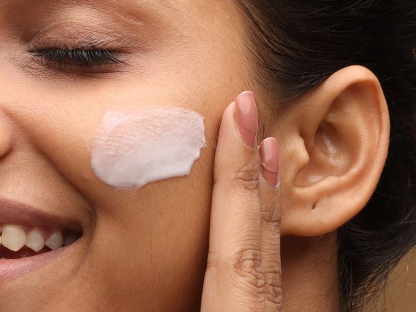 Mulher sorridente aplica um hidratante facial com textura leve e dermatológicamente testado para hidratar a pele.