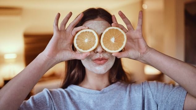 Jovem com duas rodelas de laranja fresca e vibrante em frente aos olhos.