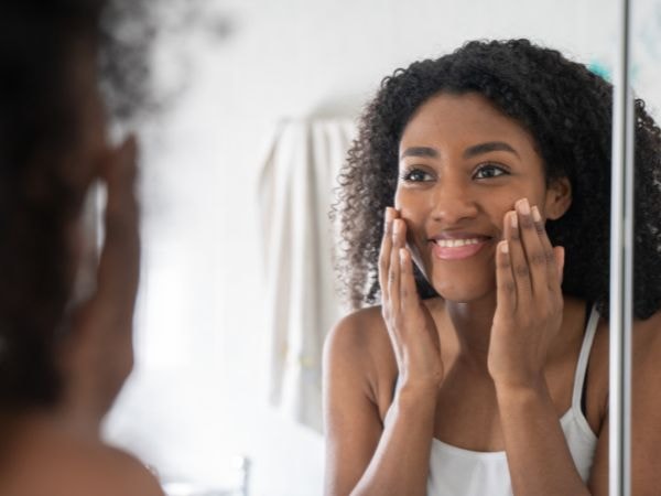 Jovem negra sorridente avalia sua pele do rosto para identificar o que pode ser e o que causa as bolinhas no rosto.