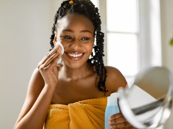 Mulher negra sorridente limpa a pele do rosto após o banho para garantir a limpeza da pele e evitar bolinhas no rosto.