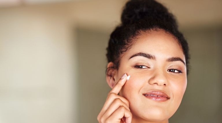 Jovem negra aplica protetor solar na pele durante tratamento para acne com isotretinoína