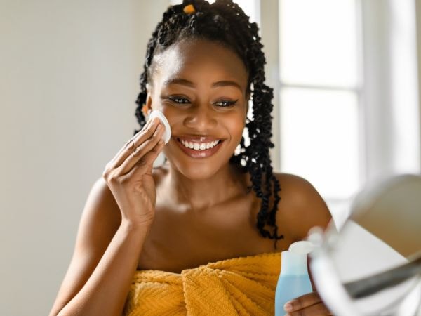 Mulher negra sorridente limpa a pele do rosto após o banho para garantir a limpeza da pele e evitar micoses.