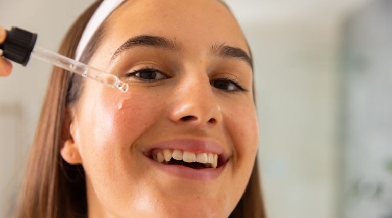 Mulher sorridente aplica um sérum em sua pele oleosa para tratar a pele facial.