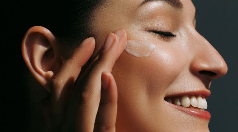 Mulher sorridente aplica o creme facial para tirar manchas no rosto