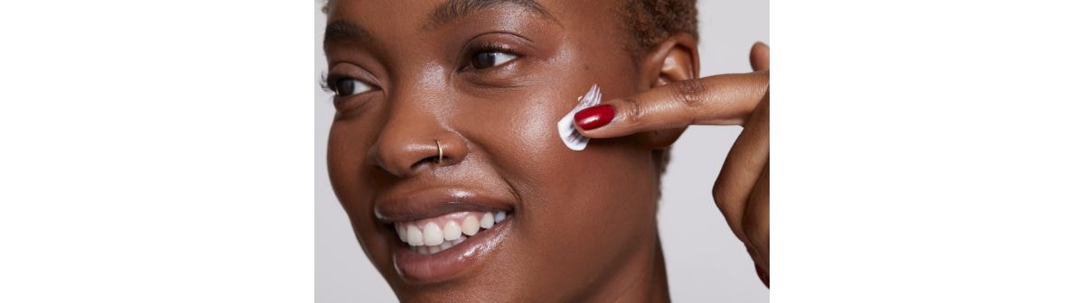 Mulher negra sorridente aplica um creme facial para manchas no rosto.