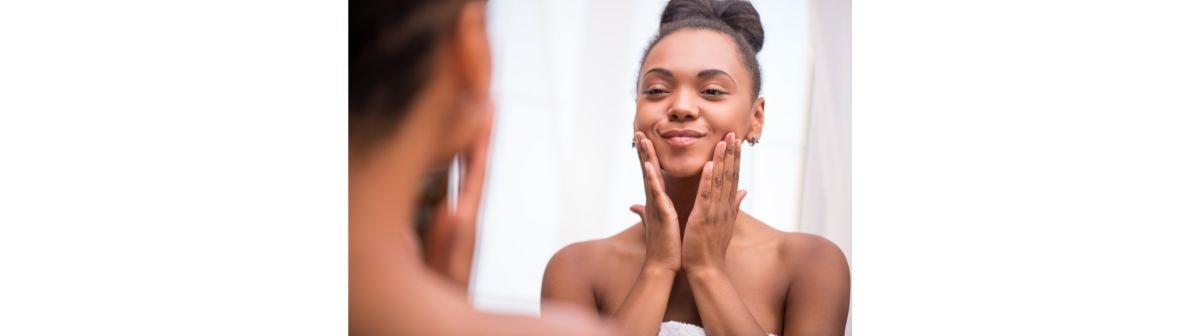 Close-up de uma pessoa com sardas aplicando delicadamente uma pequena quantidade de hidratante com niacinamida na bochecha, com um sorriso sutil, focando na aplicação do produto.