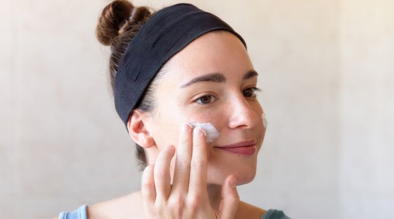 Jovem mulher aplica um hidratante para pele mista em seu rosto
