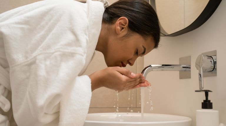 Jovem lava o rosto durante sua rotina de skincare para a pele mista