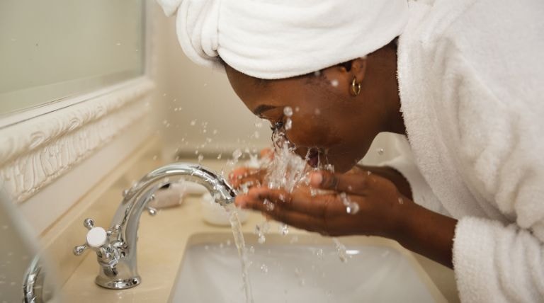 Mulher negra realiza a limpeza da pele facial antes de usar o hidratante para pele sensível