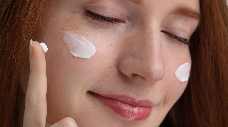 Jovem aplica um hidratante ideal para pele sensível em seu rosto