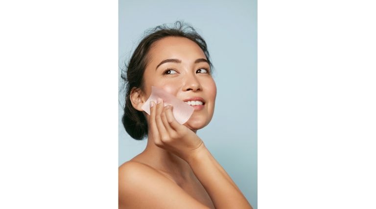 Mulher sorrindo aplicando creme facial, representando cuidados com a pele oleosa e hidratação com toque seco.